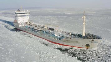 A tanker is moving along a channel among the endless ice. Drone view video