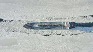 A tanker is moving along a channel among the endless ice. Drone view video