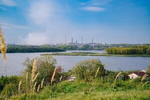 River Dividing Green Village and Factory with Large Emitting Chimneys photo