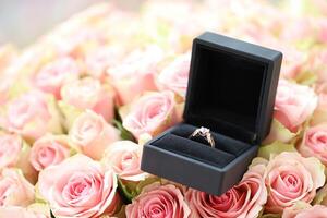 oro diamante compromiso anillo en negro caja caso entre grande cantidad de rosas en grande ramo de flores cerca arriba foto