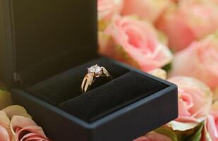 Gold diamond engagement ring in black box case among big amount of roses in big bouquet close up photo