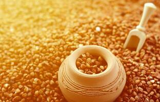 Background image of a large pile of buckwheat, in the middle of which lies a small jug and a wooden spatula for cereals photo