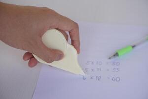 Hand use correction tape to erase incorrect numbers on paper. Concept, educational equipment, stationary item to delete or erase mistake in writing. Easy and convenient to use. photo