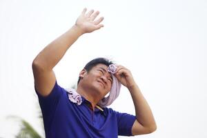 Asian man is outdoor, face up and hand up to sky, use cloth to wipe his sweat in hot weather condition. Concept, standing outdoor in hot weather is risk to heat stroke symptom. Global warming. photo