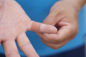 Close up man uses adhesive bandage tape to cover wound on finger. Concept, first aid. Self care for injury, to protect and prevent from dirt or germs into wound by covering adhesive bandage plaster. photo