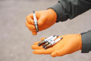 Close up mechanic hands hold old spark plug, spare part of car engine. Concept, machine maintenance, fix, repair, check or diagnose automobile problems by engine specialist. photo