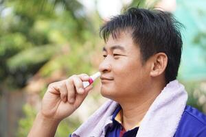 Asian man use menthol inhaler to smell for relief symptom of dizzy from hot weather condition. Concept, self first aid to protect from heat stroke. Refreshing. Aroma therapy. photo