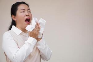 Asian woman is sneezing, open mouth, holds white tissue paper. Concept, Health problems. Ill, sick and flu. Cover mouth when cough or sneeze to stop spreading of germs, disease photo