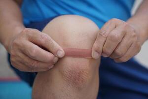 Close up man uses adhesive bandage tape to cover wound on knee. Concept, first aid. Self care for injury, to protect and prevent from dirt or germs into wound by covering adhesive bandage plaster. photo