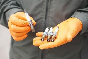 Close up mechanic hands hold old spark plug, spare part of car engine. Concept, machine maintenance, fix, repair, check or diagnose automobile problems by engine specialist. photo