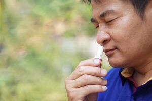 Asian man use menthol inhaler to smell for relief symptom of dizzy from hot weather condition. Concept, self first aid to protect from heat stroke. Refreshing. Aroma therapy. photo