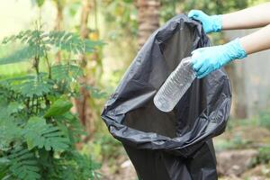 Close up hands hold plastic bottle to put in black garbage bag. Concept, garbage management, reused, recycled plastic bottles. Keep clean and community service for the best environment. Zero waste. photo