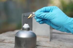 Close up hand wears blue glove, hold a burning match to light fire on alcohol lantern or laboratory lamp. Concept, equipment or tool for science experiment. Educational toolkit in science subject. photo