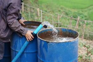 cerca arriba granjero mano sostener tubo de agua a poner dentro azul cubos en jardín. concepto, resolver problemas carente de agua en agricultura por preparar agua para riego plantas en sequía estación. foto