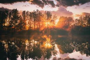 Dawn on a lake or river with a sky reflected in the water, birch trees on the shore and the sunbeams breaking through them and fog in autumn. Aesthetics of vintage film. photo