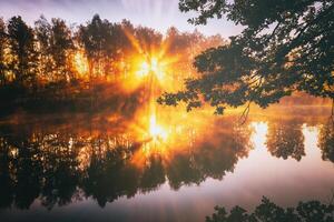 Dawn on a lake or river with a sky reflected in the water, birch trees on the shore and the sunbeams breaking through them and fog in autumn. Aesthetics of vintage film. photo