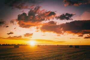 puesta de sol en el campo con pajar en otoño estación. rural paisaje con nublado cielo antecedentes en un soleado noche. Clásico película estético. foto