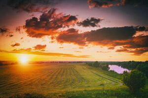 puesta de sol a cultivado tierra en el campo en un verano noche con nublado cielo antecedentes. Clásico película estético. foto