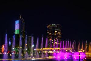 Uzbekistan, Tashkent - September 27, 2023 A fountain with laser illumination and light music in Tashkent City Park at night against the backdrop of a scyscrapers and Hilton Hotel. photo