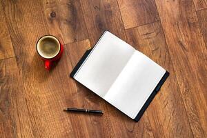 Top view of notebook with copy space for text, pen and red cup of coffee on brown table. Mock up. photo