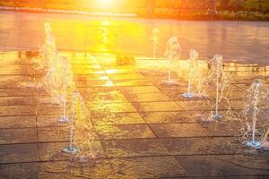 Small fountains on the sidewalk, illuminated by sunlight at sunset or sunrise at summertime. photo