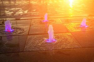 Small fountains on the sidewalk, illuminated by sunlight at sunset or sunrise at summertime. photo