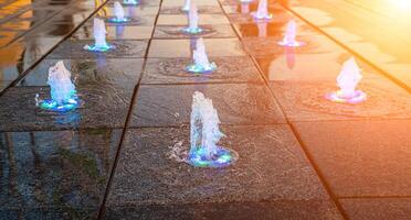 Small fountains on the sidewalk, illuminated by sunlight at sunset or sunrise at summertime. photo
