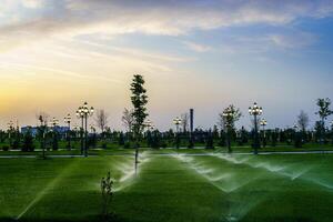 City park in early summer or spring with lanterns, young green lawn, trees and dramatic cloudy sky on a sunset or sunrise. photo