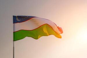 Flag of Uzbekistan waving on a sunset or sunrise dramatic sky background. photo