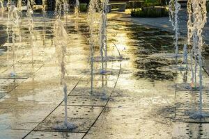 Small fountains on the sidewalk, illuminated by sunlight at sunset or sunrise at summertime. photo