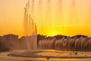 Big fountains on the artificial pond, illuminated by sunlight at sunset in Tashkent city park at summertime. photo