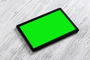 Black tablet with green screen on a wooden table mock up. Copy space chroma key display. photo