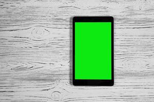 Black tablet with green screen on a wooden table mock up. Copy space chroma key display. photo