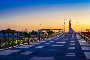 UZBEKISTAN, TASHKENT - APRIL 25, 2023 The territory of the park New Uzbekistan with Monument of Independence in the form of a stele with a Humo bird at twilight. View from a bridge. photo