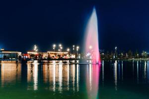 Blurred fountain water flows in an artificial lake in a night park with lanterns and decorations. photo