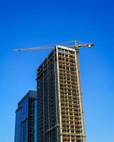 A crane building a modern skyscraper against a blue sky. Construction site. photo