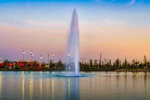 Blurred fountain water flows in an artificial lake in a evening park with lanterns and decorations at twilight. photo
