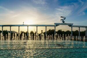 Memorial and rows of fountains illuminated by sunlight at sunset or sunrise in the Independence Square at summertime, Tashkent. photo