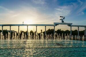 monumento y filas de fuentes iluminado por luz de sol a puesta de sol o amanecer en el independencia cuadrado a Hora de verano, Taskent. foto