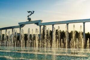 Memorial and rows of fountains illuminated by sunlight at sunset or sunrise in the Independence Square at summertime, Tashkent. photo