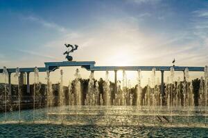 monumento y filas de fuentes iluminado por luz de sol a puesta de sol o amanecer en el independencia cuadrado a Hora de verano, Taskent. foto