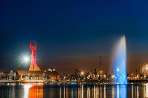 UZBEKISTAN, TASHKENT - APRIL 25, 2023 Illuminated monument of independence in the form of a stele with a Humo bird and fountain in the New Uzbekistan park at nighttime. photo