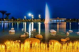 Blurred fountain water flows in an artificial lake in a night park with lanterns and decorations. photo
