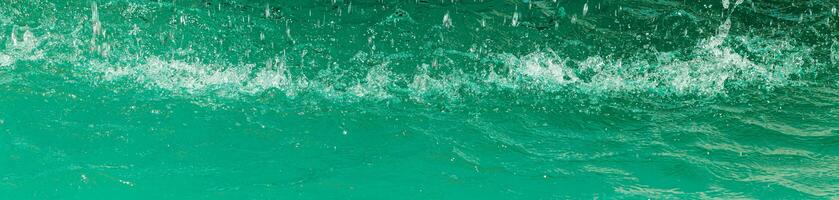 Turquoise flow of falling water and splashes from it, illuminated by sunlight. Nature background. photo