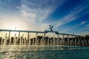 Memorial and rows of fountains illuminated by sunlight at sunset or sunrise in the Independence Square at summertime, Tashkent. photo