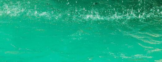 Turquoise flow of falling water and splashes from it, illuminated by sunlight. Nature background. photo