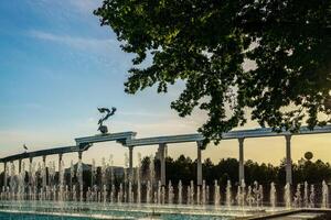 monumento y filas de fuentes iluminado por luz de sol a puesta de sol o amanecer en el independencia cuadrado a Hora de verano, Taskent. foto