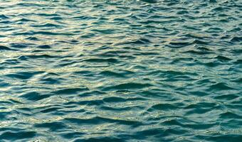 el textura de el olas en turquesa color, iluminado por el Dom a puesta de sol o amanecer. naturaleza antecedentes. foto