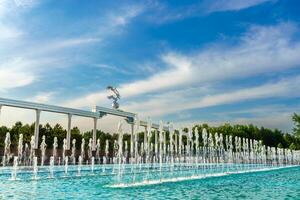 Memorial and rows of fountains illuminated by sunlight at sunset or sunrise in the Independence Square at summertime, Tashkent. photo