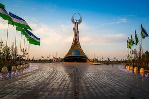 UZBEKISTAN, TASHKENT - MAY 5, 2023 Fountains in a background of monument of Independence in the form of a stele with a Humo bird and waving flags on a sunset after rain in the New Uzbekistan park. photo